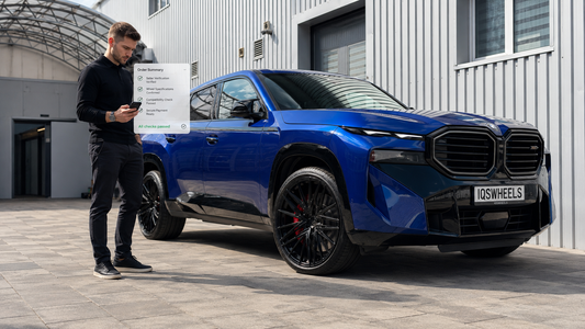 Customer verifying a custom wheel seller before payment, next to a real vehicle fitted with custom forged wheels